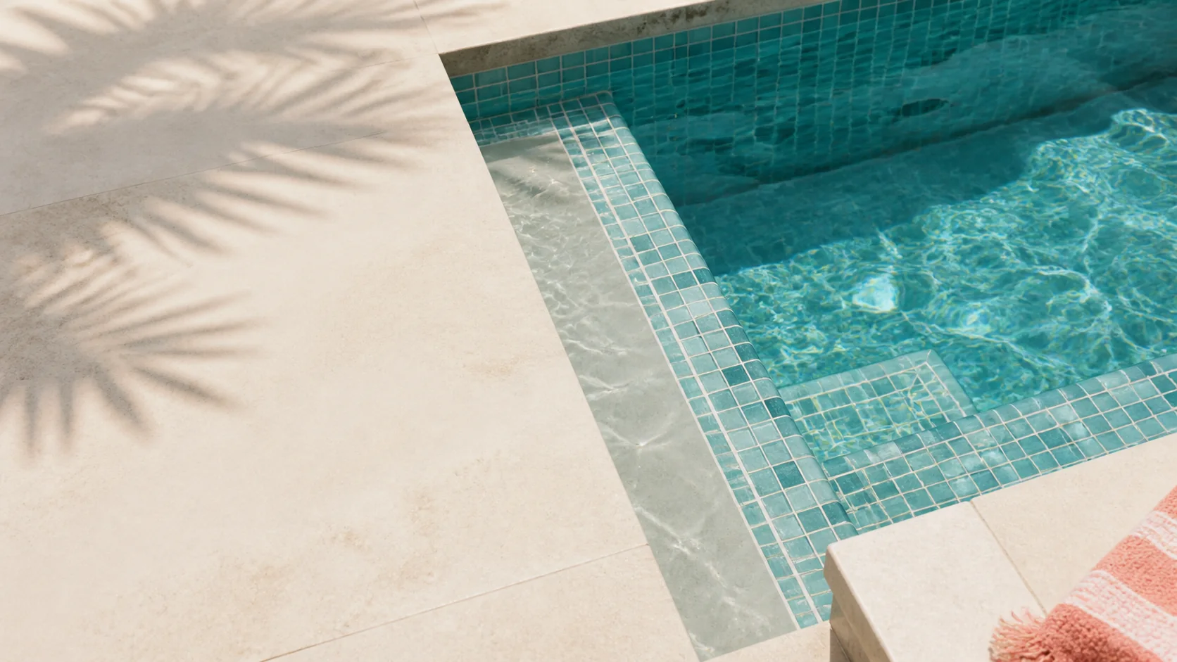 Sunlit turquoise pool waterline and pale stone deck